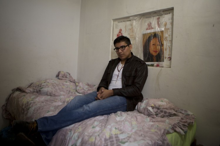 In this Friday, Oct. 3, 2014 photo, Dario Guerrero sits for a portrait in his bedroom with a picture of his late mother, at his grandparents’ home on the outskirts of Mexico City. Guerrero, a Harvard University junior, accompanied his dying mother to Mexico without government permission, and is now unable to return to the United States.
