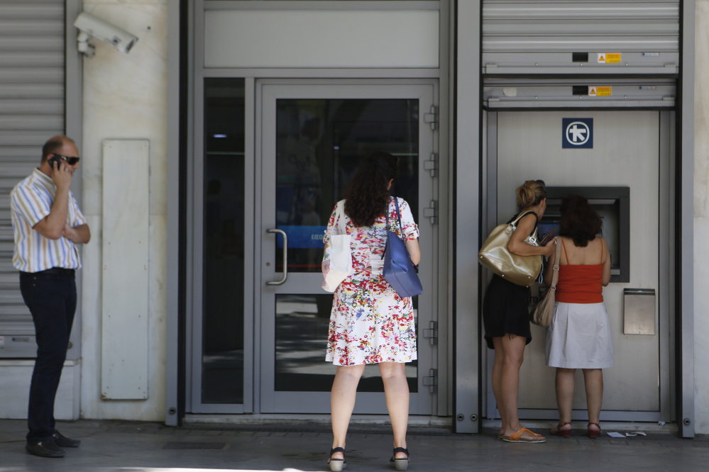 Women use an ATM machine, as others wait outside a closed bank in Athens on Wednesday. All 28 leaders of the full European Union will meet on Sunday in what has been called Greece’s last chance to stay in the euro. Meanwhile, Greeks cannot withdraw more than 60 euros ($67) a day from an ATM, and bank closures were extended into next week.